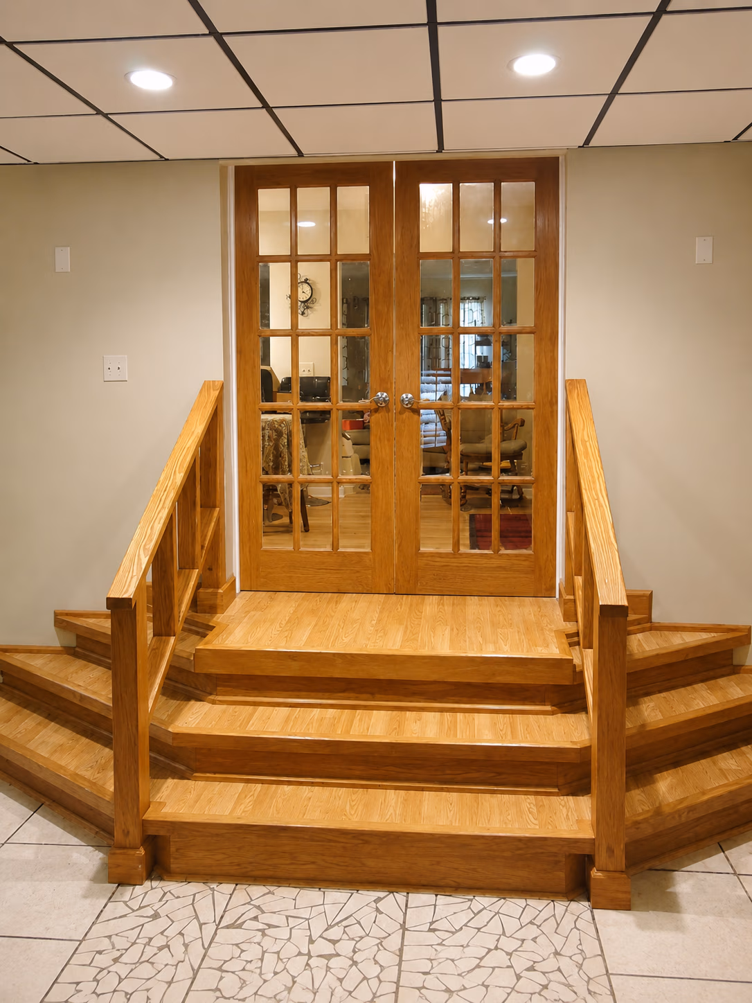 Wooden staircase with handrails leads to double glass-paneled doors revealing a cozy room inside.