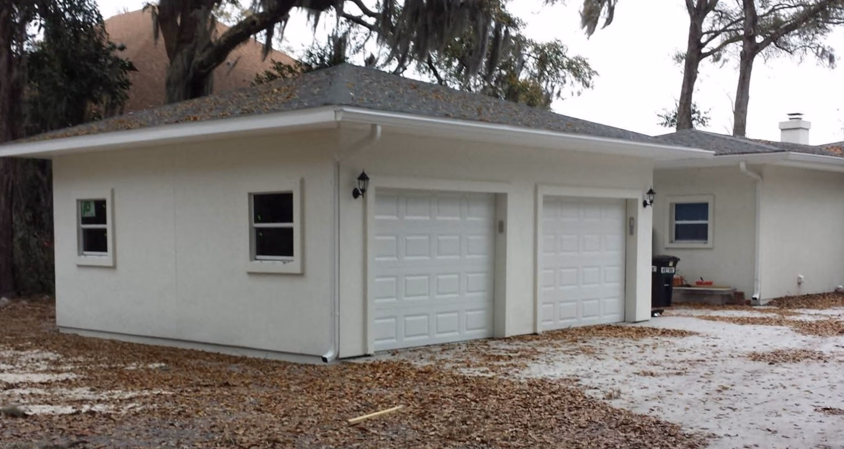 Single-story beige building with two closed garage doors and fallen leaves on the ground.