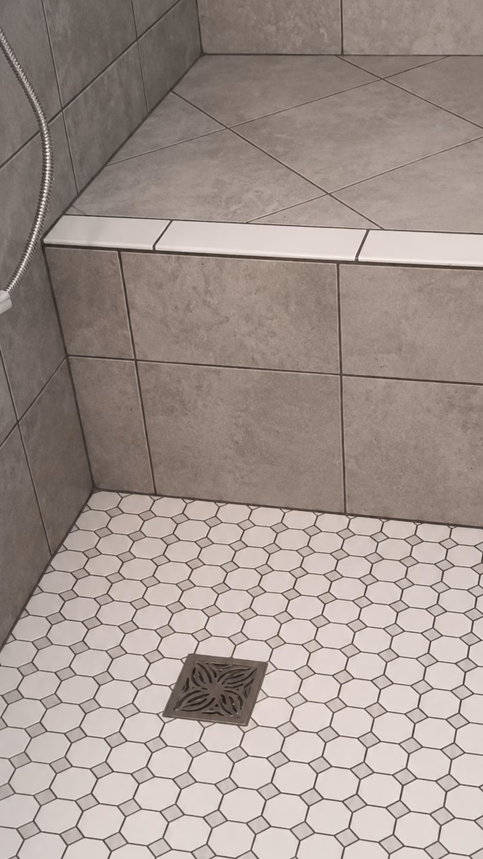 Corner of a tiled shower with a built-in bench and a decorative square floor drain.
