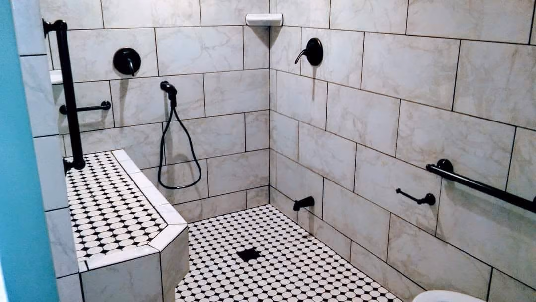 Accessible shower with built-in bench, grab bars, hand shower, and tiled walls and floor.