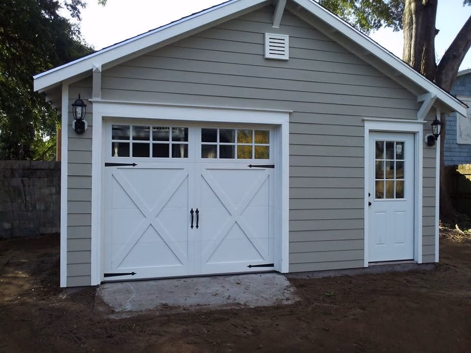 Gray garage with white double doors featuring cross design and a white side door with window panes.