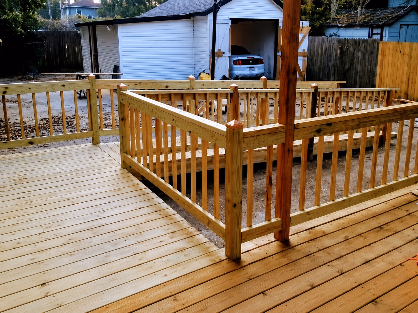 Wooden deck and ramp railing beside a white garage with a parked car inside.