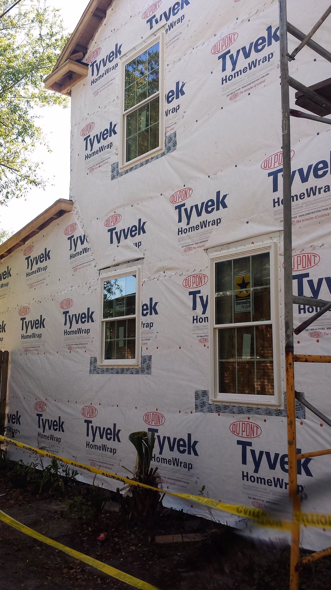 House exterior covered in DuPont Tyvek HomeWrap with three windows and yellow caution tape around the site.