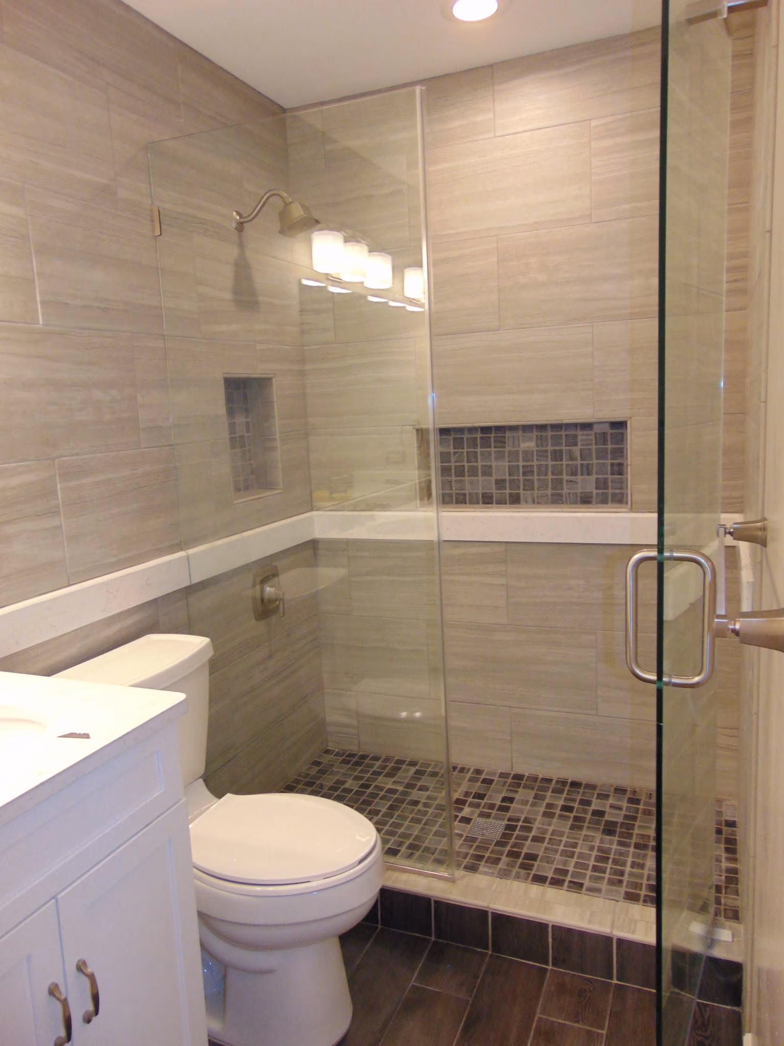 Modern bathroom with white toilet, glass shower with tiled floor and walls, and vanity cabinet.