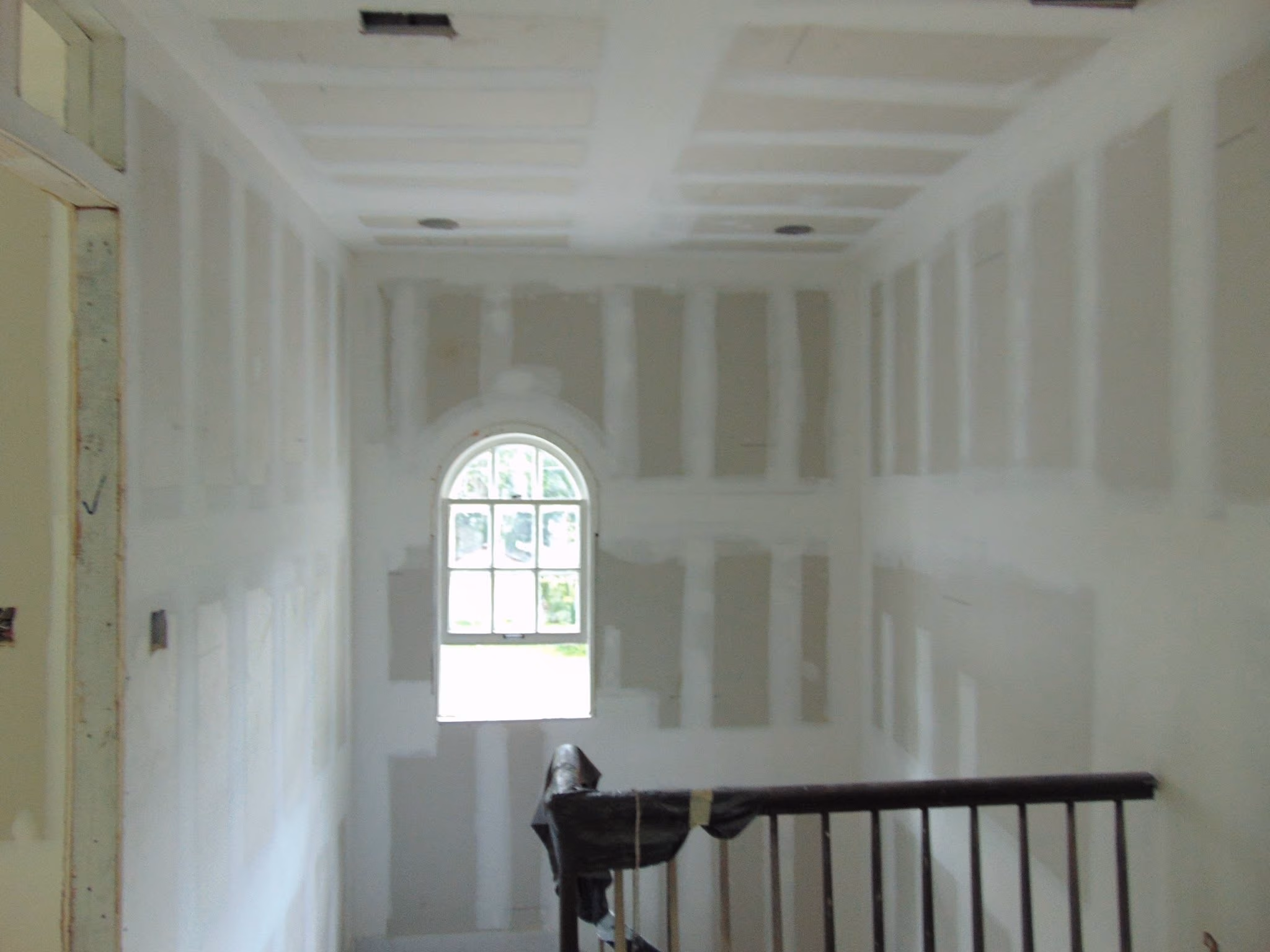 Interior stairwell under construction with drywall and an arched window letting in light.