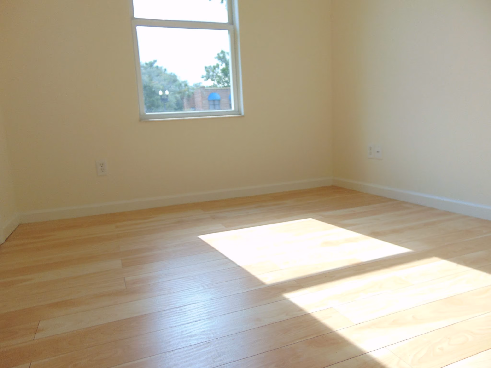 Empty room with light wood floor, beige walls, and sunlight through a window casting a square shape.