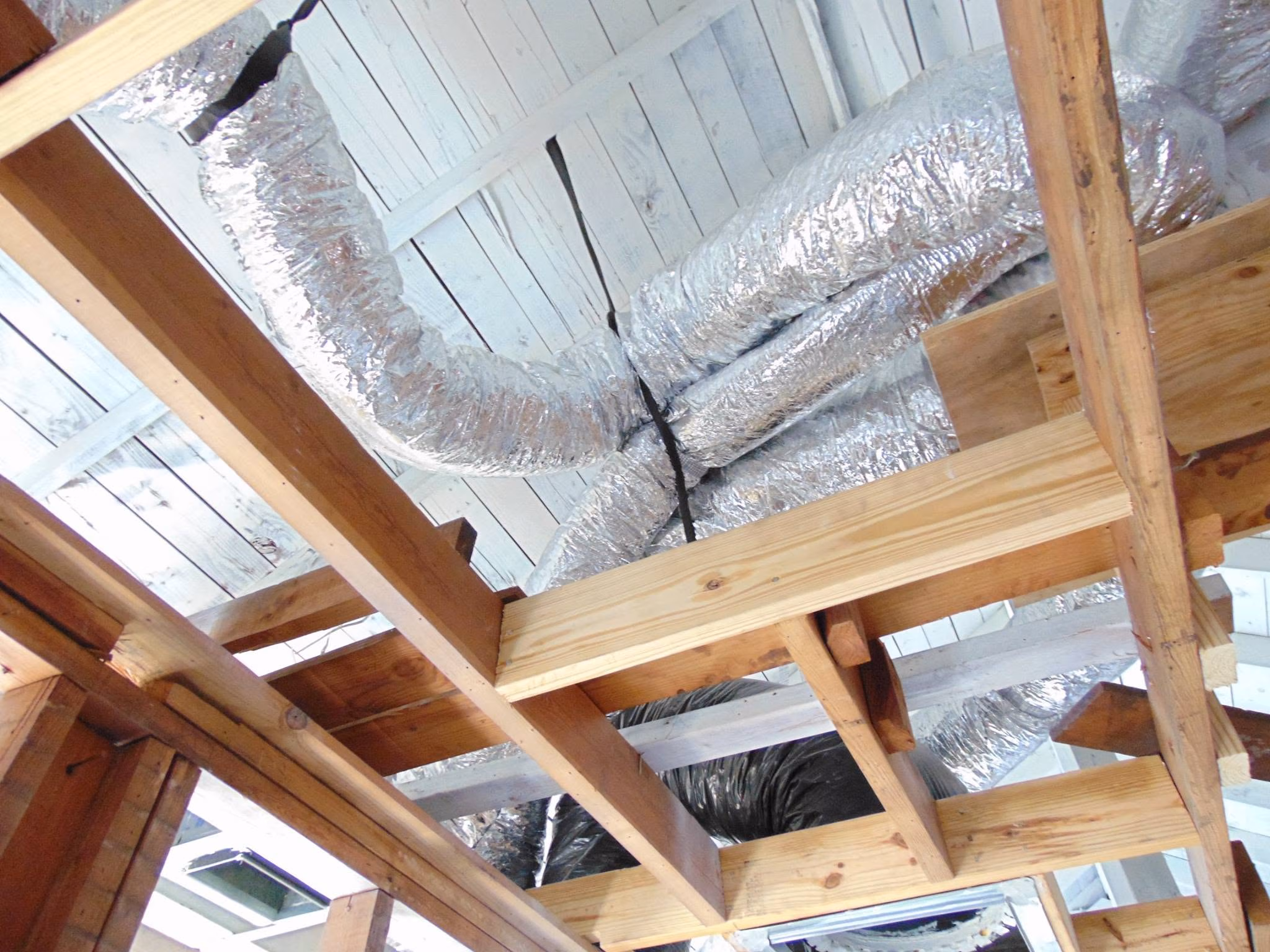 Exposed wooden ceiling framing with insulated silver air ducts in an unfinished building interior.