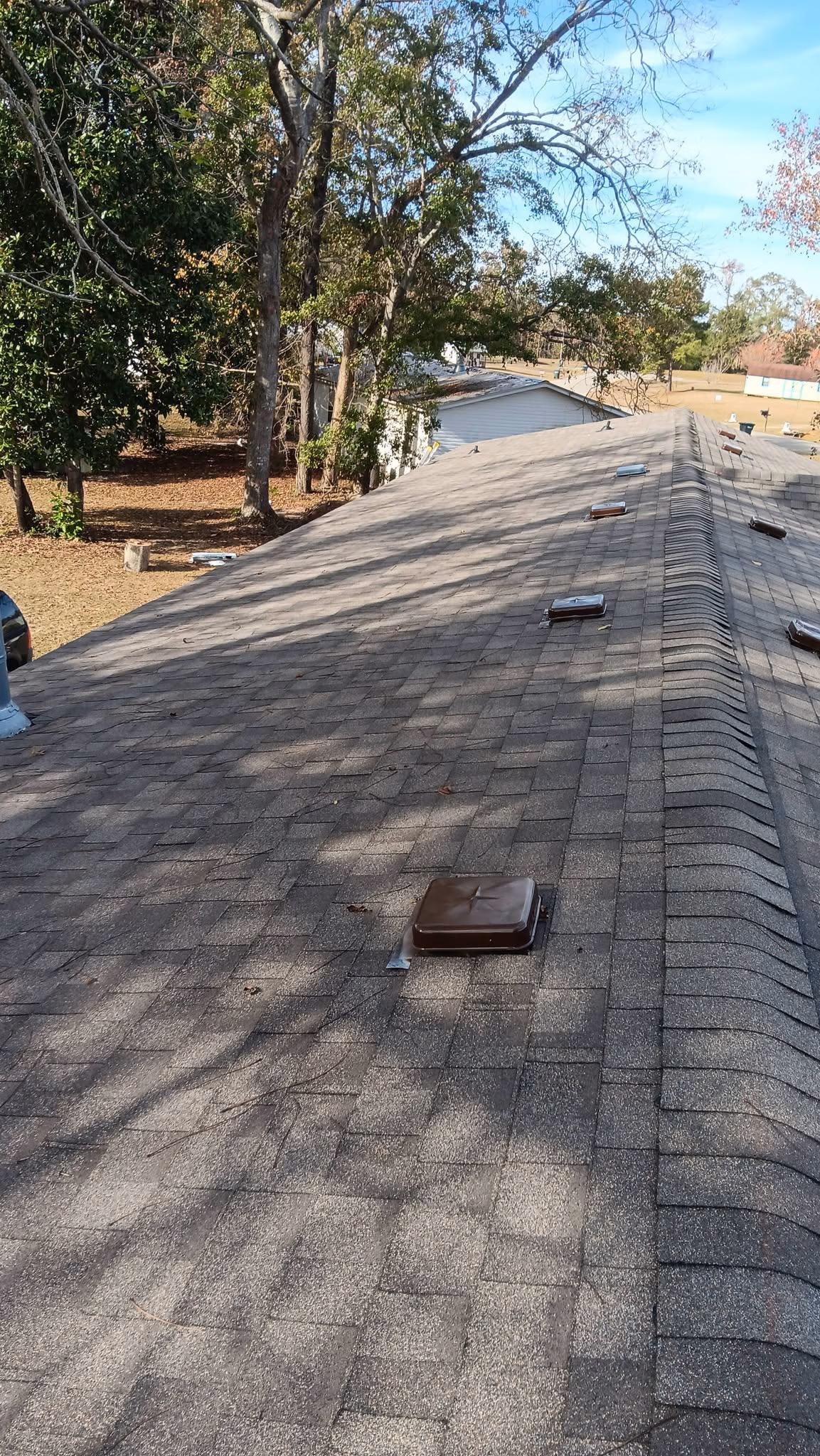 Shingled roof with multiple brown square vents and trees in the background on a sunny day.