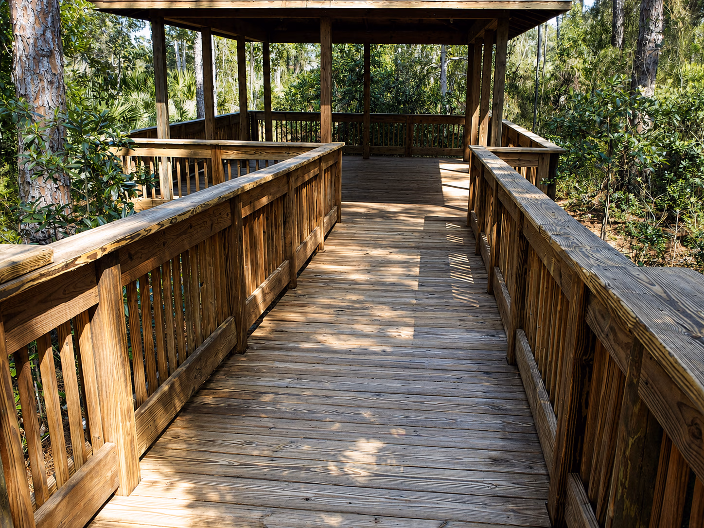 Wooden boardwalk with railings leads to a covered lookout surrounded by green trees and foliage.