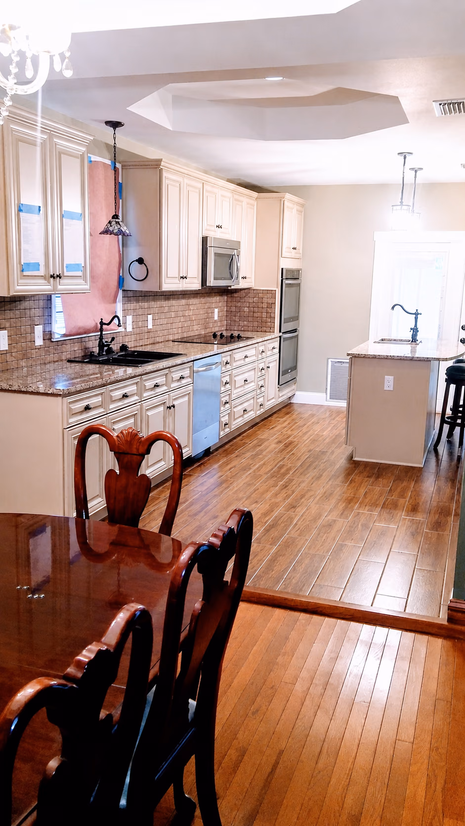 Bright kitchen with wooden floors, cream cabinets, granite counters, and dining table with wooden chairs.