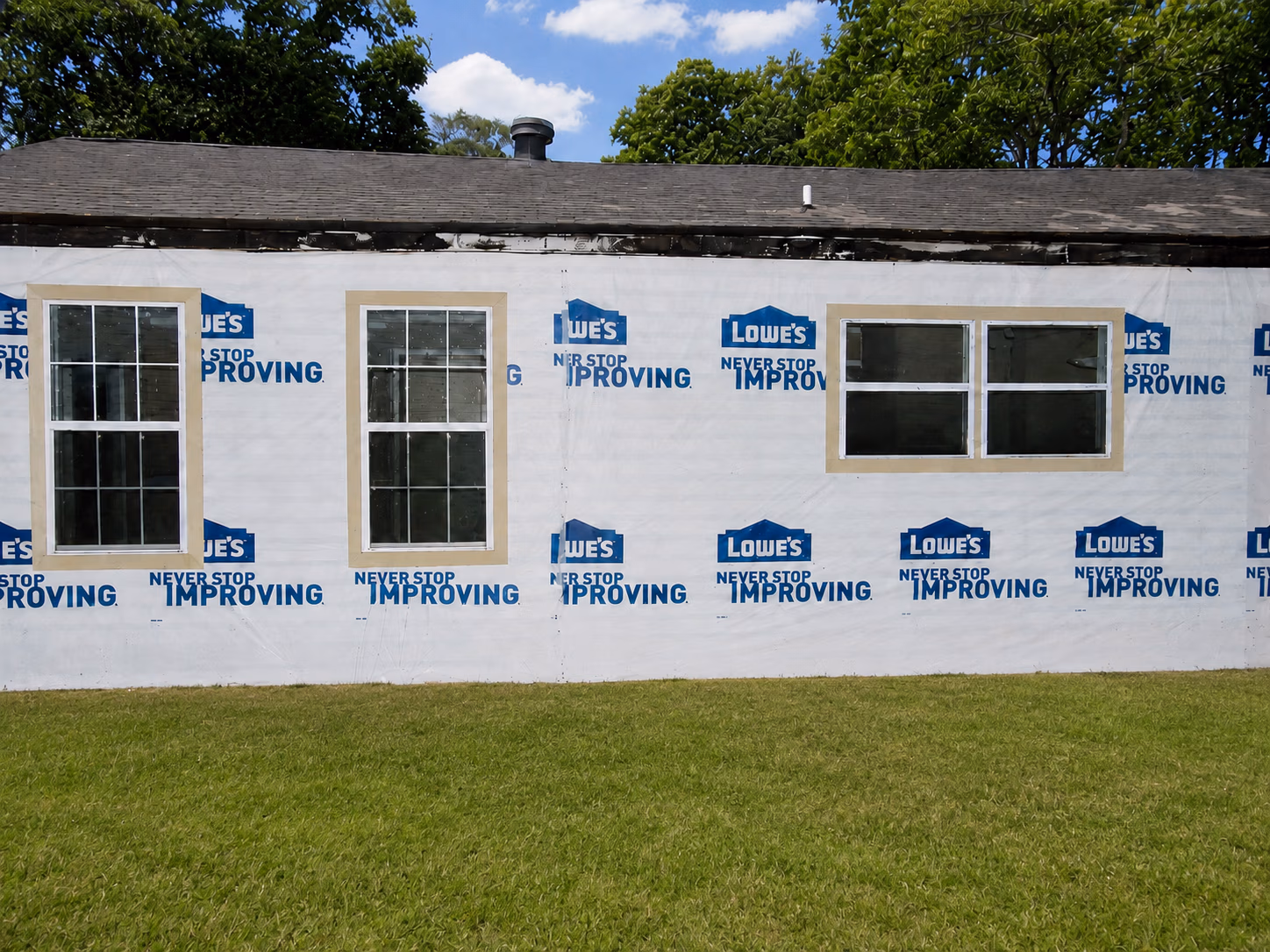 House under construction with three white framed windows and Lowe's branded house wrap.