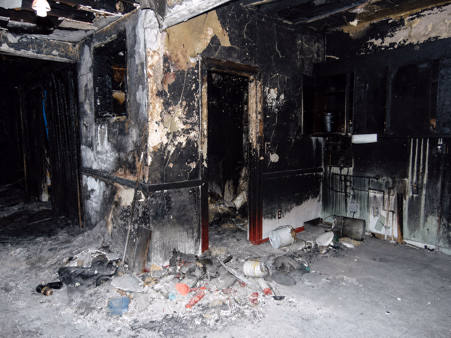 Room severely damaged by fire with charred walls and debris scattered on the floor.