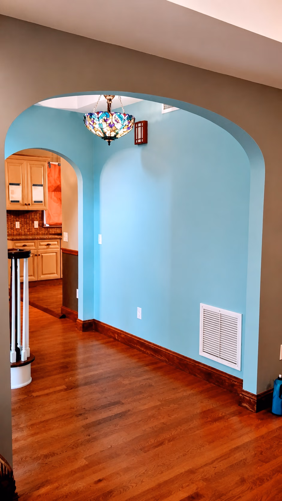 Empty hallway with blue walls, wooden floor, an archway, and a stained glass hanging light.