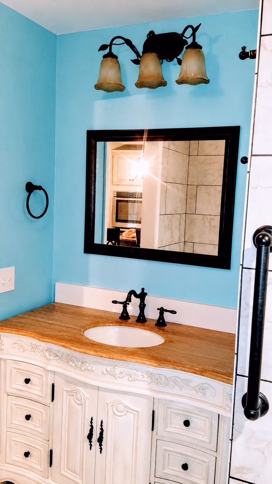 Bathroom vanity with wooden countertop, white sink, black faucet, mirror, and blue walls.