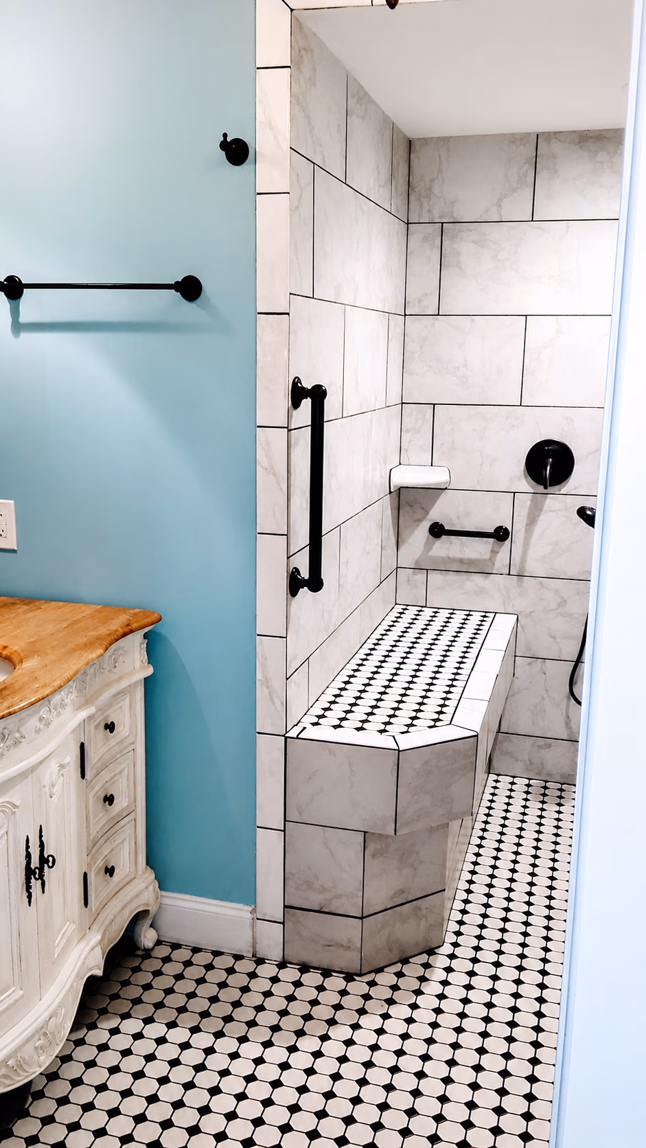 Bathroom with marble tile walk-in shower, built-in bench, black grab bars, and vintage wood vanity.