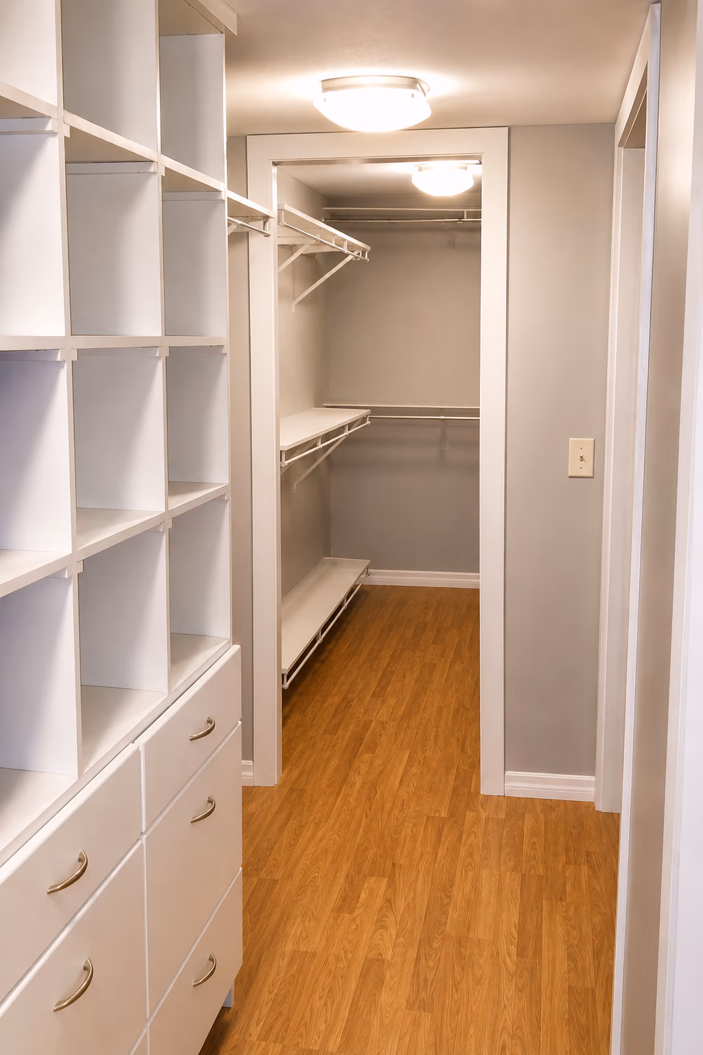 Empty walk-in closet with white shelves, drawers, hanging rods, and wooden floor.