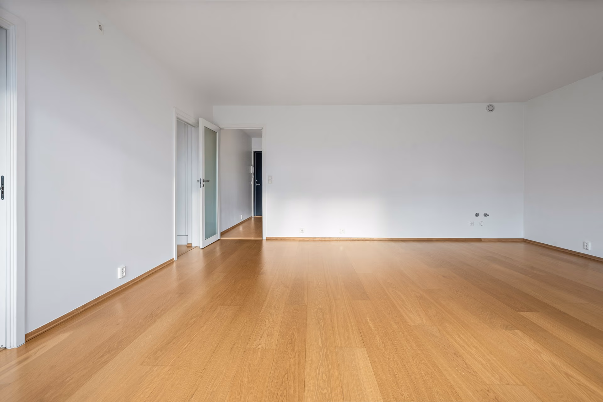 Empty room with light wood flooring, white walls, and an open door leading to a hallway.