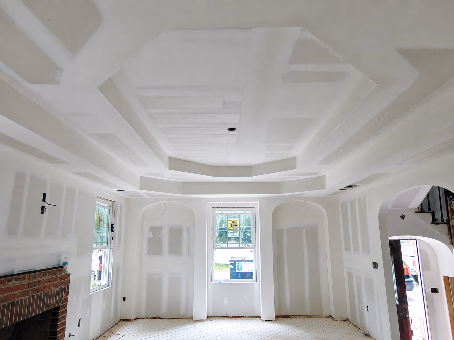 Room under construction with drywall unfinished, windows, a brick fireplace, and an ornate recessed ceiling.