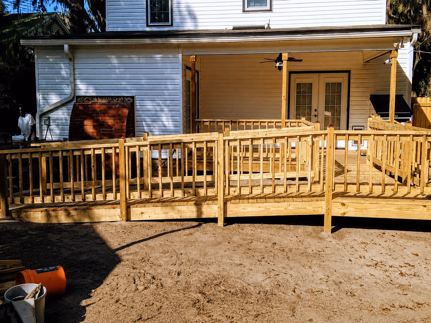 Wooden wheelchair-accessible ramp leading to a house patio with white siding and double doors.