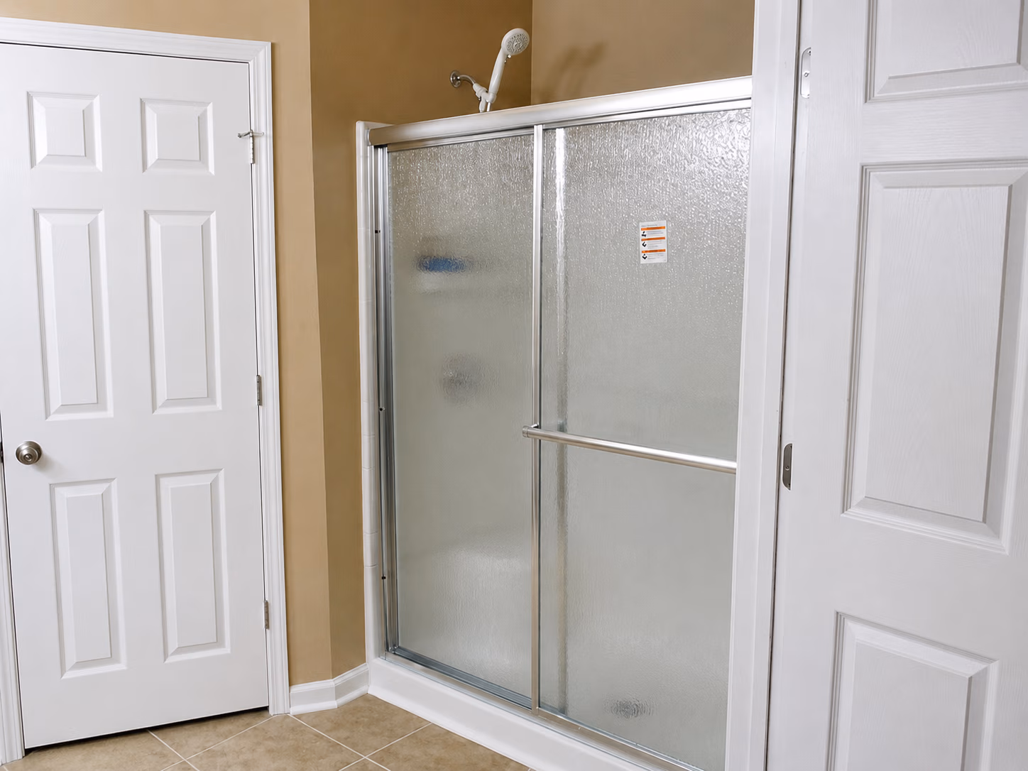 Bathroom corner with beige walls, white doors, tiled floor, and glass shower enclosure with sliding doors.
