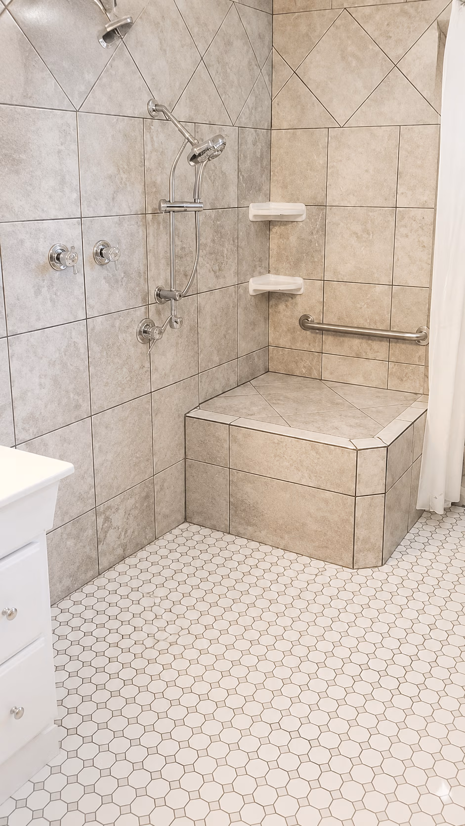 Shower area with tiled walls, built-in bench, grab bar, showerhead, and hexagonal tiled floor.