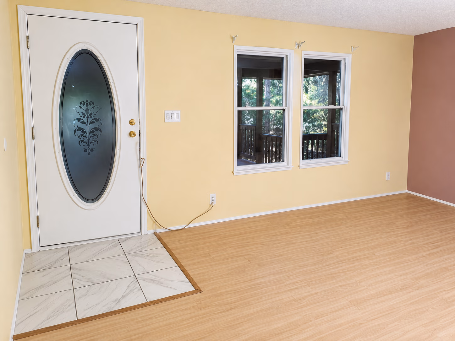 Empty room with yellow walls, wood floor, white door with frosted glass oval, and two windows.