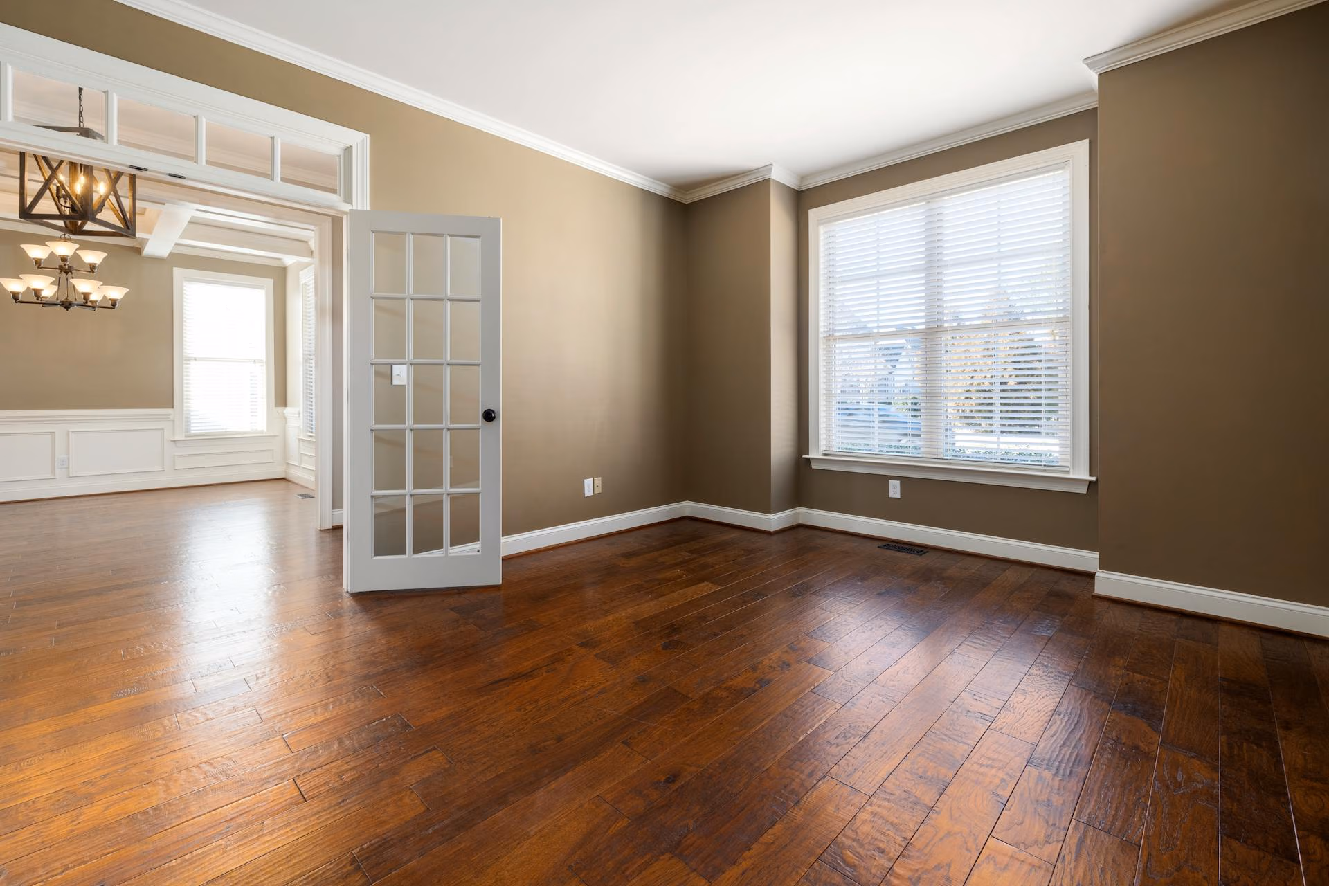Empty room with brown walls, hardwood floors, a window with blinds, and a glass-paneled door.