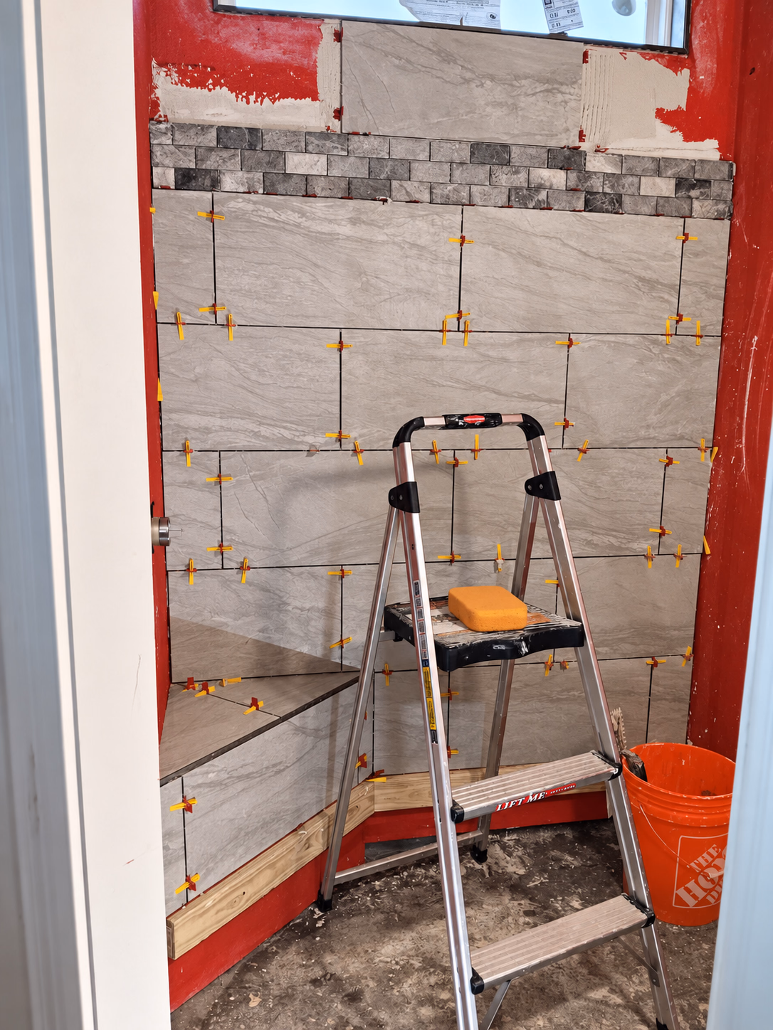 Large shower wall tiles being set with leveling spacers, a step ladder in front